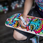 Person dekorerer et skateboard med et farverigt, komplekst mønster ved hjælp af en rød Sharpie tusch.