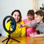 Tre piger bruger V-TAC LED-ringlyset med bordstativ og mobilholder ved et bord.