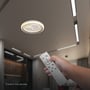 En hånd retter fjernbetjeningen mod den tændte V-TAC LED-loftslampe i loftet.