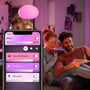 Philips Hue Flourish-pendel lyser pink over et par, der styrer flere Hue-lamper via en telefon.