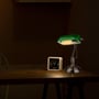 V-TAC skrivebordslampe med grøn glasskærm, der lyser op på et træbord med et ur ved siden af.