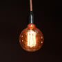 Tændt G125 LED kultrådspære i ravfarvet glas, monteret i en lampe med stofledning mod mørk baggrund.