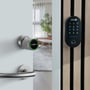 Zafe smart-cylinder OVAL med app monteret på en lys dør ved siden af et sort Zafe-kodepanel med taster.