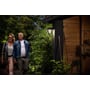 Philips Lighting Alpenglow Down væglampe i sort aluminium monteret på en mørk stolpe, oplyser en havegang med to personer til venstre.