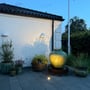 Light By Juul Opal nedgravningsspot lyser varmt fra terrassefliserne i en have ved skumring.