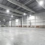Et stort lagerlokale med betongulv og højt til loftet, belyst af flere V-TAC LED højby lamper.