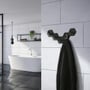 Smedbo Beslagsboden hexagon enkeltkroge monteret på en grå flisevæg i et moderne badeværelse med et sort håndklæde hængende.