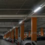 Række af V-TAC 120 cm LED armaturer monteret i et parkeringshus med orange søjler og parkerede biler.