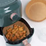 Nærbillede af sprøde nuggets i Nordic Quality rundt bagepapir i en grøn airfryer kurv, med bagepapir og kager ved siden af.
