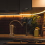 V-TAC LED stripelys monteret under køkkenskabe som indirekte belysning med varmt, gyldent skær, der fremhæver flisbagvæggen.
