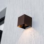 V-TAC 9W LED væglampe med corten hus, monteret på en hvid, tekstureret murstensvæg, lysende nedad.