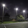 Tre kraftige V-TAC LED projektører monteret på høje master oplyser en tennisbane i mørke.