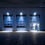 V-TAC LED-projektører lyser over tre industriporte og oplyser pladsen foran bygningen i mørke.