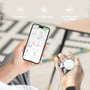 En hånd holder nøgler med den hvide 4smarts SkyTag Duos lokaliseringsfinder, mens en telefon viser et kort.