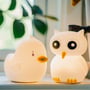 Sød Star Trading LED børnelampe formet som en ugle i hvid plast, der lyser blødt og står ved siden af en andelampe.