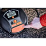 Osram TYREinflate 6000 dækoppumper, hvor en finger trykker på power-knappen, med fokus på kontrolpanelet og orange detaljer.