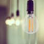 V-TAC E14 LED-kronepære P45 hænger tændt i en fatning med synlige filamenter og varm glød.