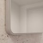 Loevschall Refine spejl med en ramme i børstet aluminium, vist på en rå, stenlignende væg, der fremhæver spejlets moderne design.