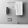 Knud Holscher toiletrulleholder fra d line ses monteret uden rulle blandt badeværelsestilbehør på grå væg.