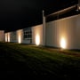 Light By Juul Gold nedgravningsspot i brug om aftenen, hvor varmt lys fra jorden oplyser en bygningsfacade.