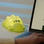 Mochi krokodille-natlampe lyser varmt gult ved siden af en bærbar computer.