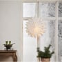 Star Trading papirstjerne, 60 cm, hænger i et vindue ved siden af en potteplante og julelys, skaber hygge.