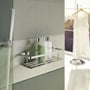 Smedbo Sideline brusekurv i poleret krom med to flasker shampoo, vist på et moderne badeværelsesvæg.