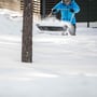Fiskars Snowexpert sneslæde i brug på snefyldt område med person i blå jakke, der rydder sne.