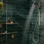 Brusekabine med Hansgrohe opbevaringskurv, brusehoved og en brusebadsarmatur på en mørkegrøn flisevæg.