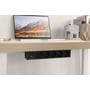 Deltaco under-skrivebord strømskinne med 5 stik og 2 USB-porte monteret under et lyst træskrivebord med en bærbar computer.