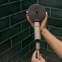Hænder der samler en beige Hansgrohe håndbruserslange på 1,6 meter med et gråt håndbruserhoved med SELECT-knap.