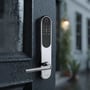 Zafe T-Lock oval dørlås med sort tastatur og rustfri front monteret på en mørk dør med vanddråber.
