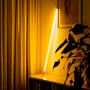 LEDlife Neon Tube LED, 120 cm, gul, lyser skråt op ad et skab ved gardiner og en plante.
