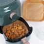 Detaljebillede af Nordic Quality firkantet airfryer bagepapir, et med friturestegt kylling i en airfryer og et tomt.