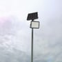 V-TAC 120W LED solar projektør med tilhørende solpanel monteret på en høj mast mod en overskyet himmel.