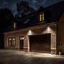 Noctis Lux 4 projektør monteret på murstensfacade over garage, oplyser indkørsel med varm hvidt lys.