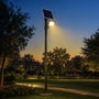 V-TAC LED-projektør med solcellepanel lyser fra en mast i en park ved skumring.