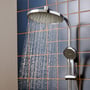 Hansgrohe Activera S Showerpipe 240 med vand der løber fra både hovedbruser og håndbruser mod en mørkeblå kakkelvæg.