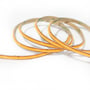 COB-LED-strip Anycut ligger i overlappende buer, så den smalle orange bagside og stripprofilen ses tydeligt.