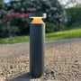 Light By Juul Platin slim pullert lyser varmhvidt i en grusbelagt have, set tæt forfra.
