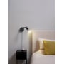 Astro Lighting Ascoli Swing Plug In væglampe i mat sort monteret ved en seng, hvor den lyser ned over sengegærdet.