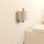 Forkromet LAUFEN Niara reservepapirholder monteret på en badeværelsesvæg med en toiletrulle.