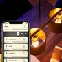 Philips Hue E14 LED-kertepære styres i Hue-appen på en telefon ved siden af varmt lysende pendellamper.