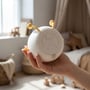 En hånd holder MOCHI natlampen med undersiden vendt frem, så betjeningsknap og indstillinger er synlige.