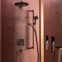 Hansgrohe Raindance Alive S håndbruser i mat sort, vist i brug med brusehoved, der sender PowderRain stråler mod en rustik væg.