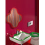 Laufen FLORA KIDS børnespejl monteret på en rød væg over et grønt og hvidt håndvask, med synlig toilet og tilbehør.