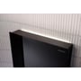 Geberit Monolith Plus cisternemodul i sort, monteret på en badeværelsesvæg med hvide, aflange fliser, oplyst med integreret LED-lys.