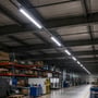 Flere V-TAC LED-armaturer lyser langs loftet i et stort lager med reoler og arbejdsområder.
