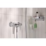 Grohe Swift brusearmatur i krom med blank overflade, monteret på hvid væg ved siden af en hylde med sæbe.