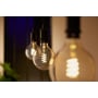 Philips Hue G125 Globe-filamentpære hænger tændt i en fatning blandt andre dekorative globepærer.